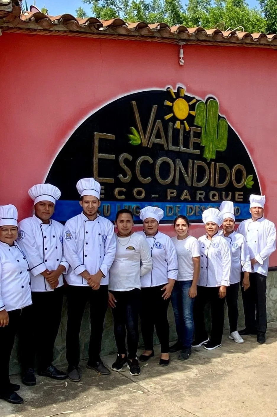 Grupo de cocineros con uniformes y gorros frente a cartel que dice Valle Escondido en un parque ecológico.