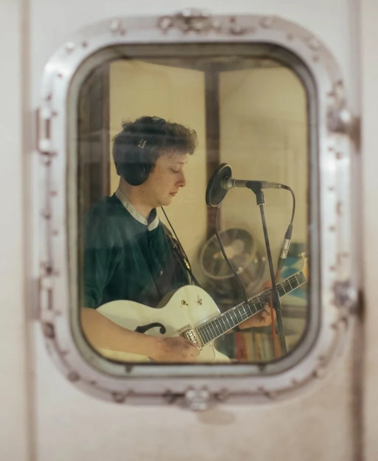 View through the window into the vocal booth whilst a musician performs inside