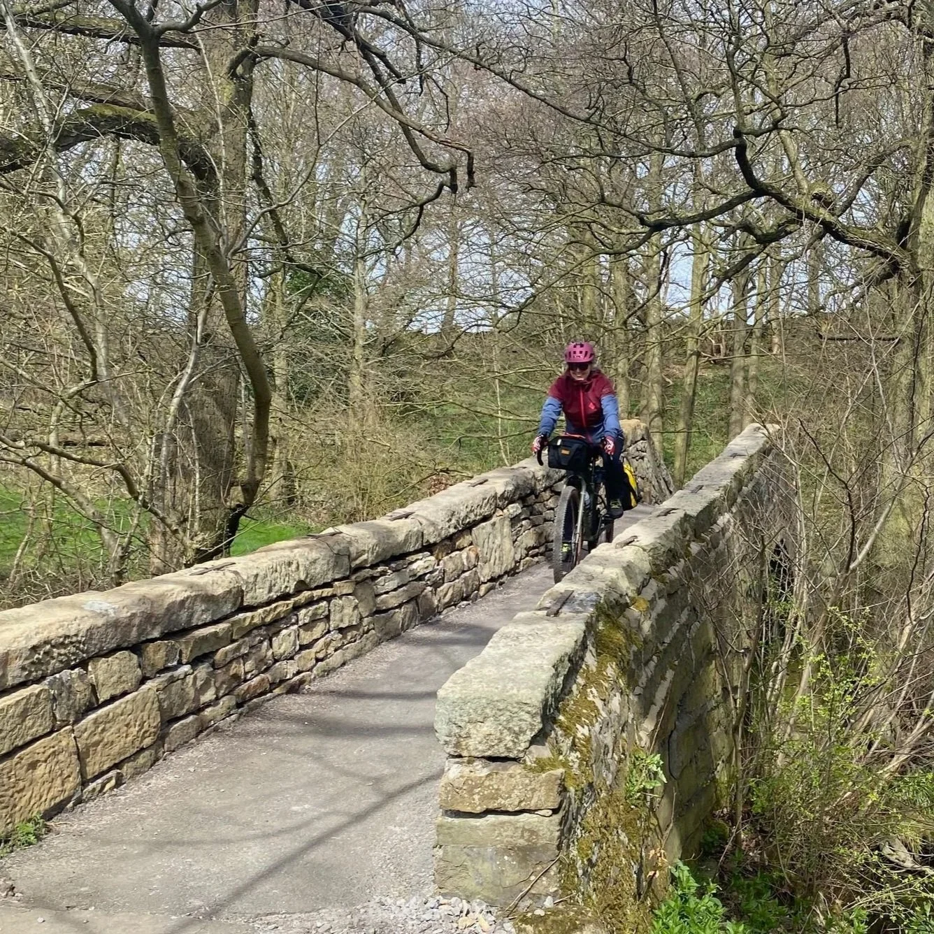Jacquie Budd cycling over an old stone packhorse bridge