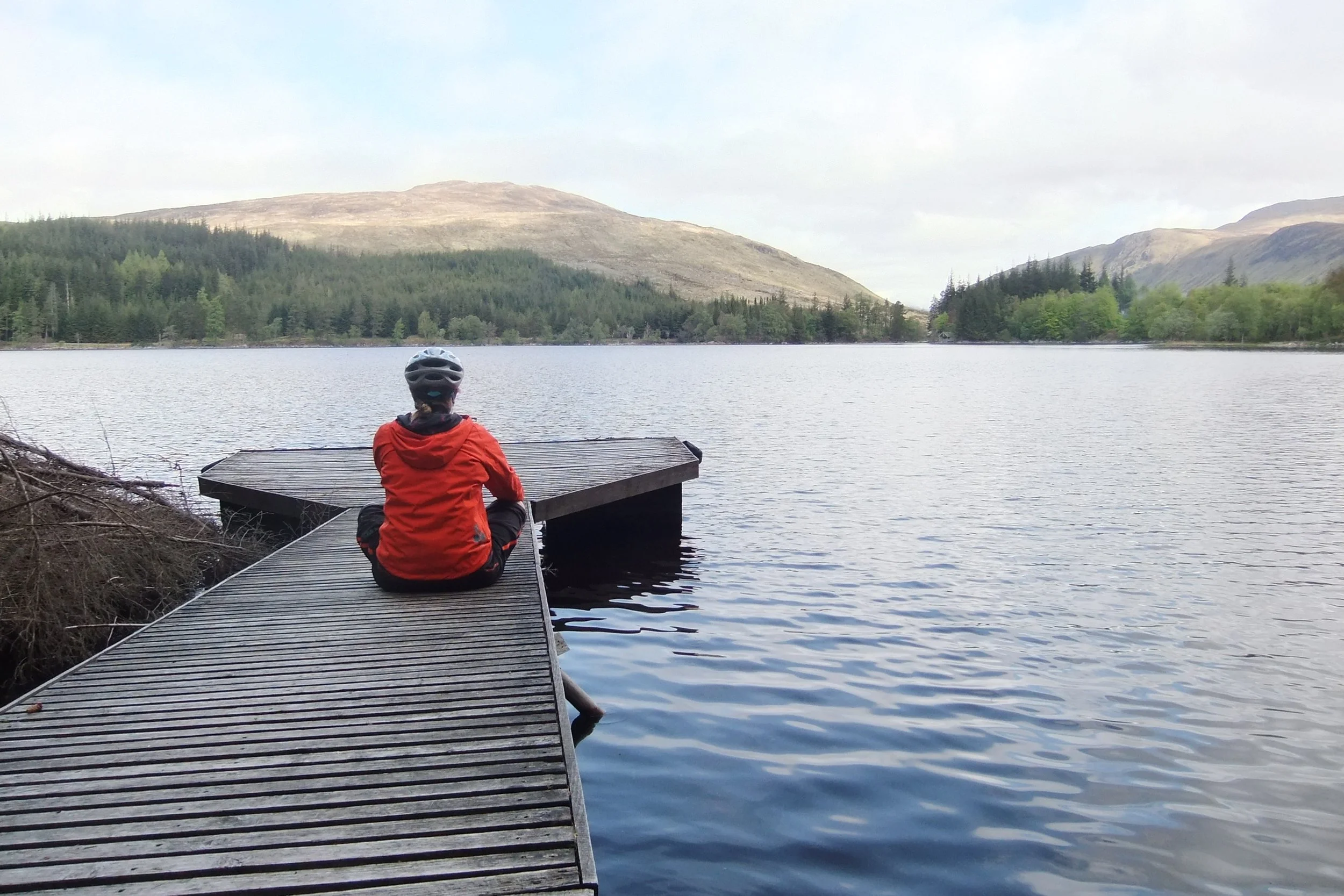 Jacquie Budd sitting on a dock looking out across Loch Ossian, Scottish Highlands