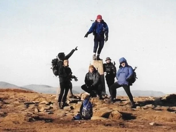 Walkers surrounding a trig point on High Street summit, Lake District National Park