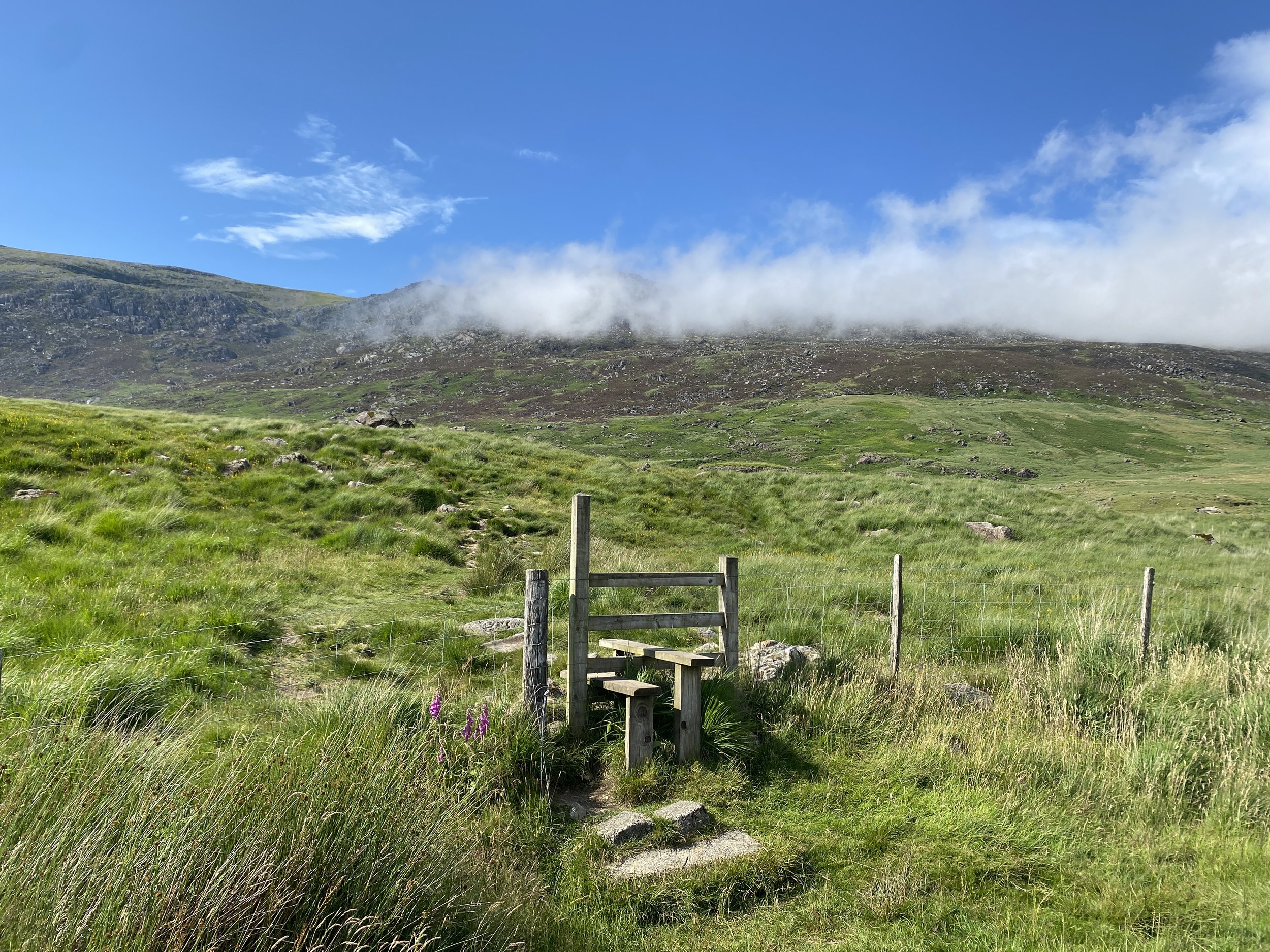 Wooden style leading to open countryside in Snowdonia, with low cloud and blue sky
