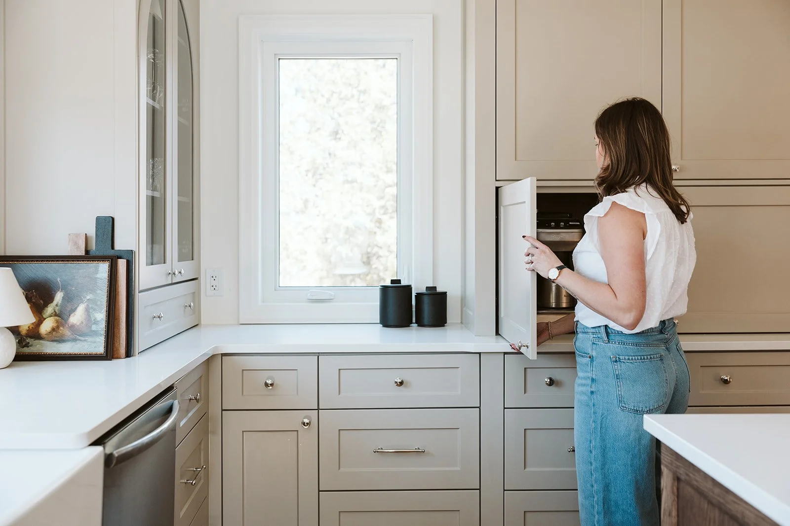 Kitchen design with functional light beige millwork and the interior designer opening the appliance garage.