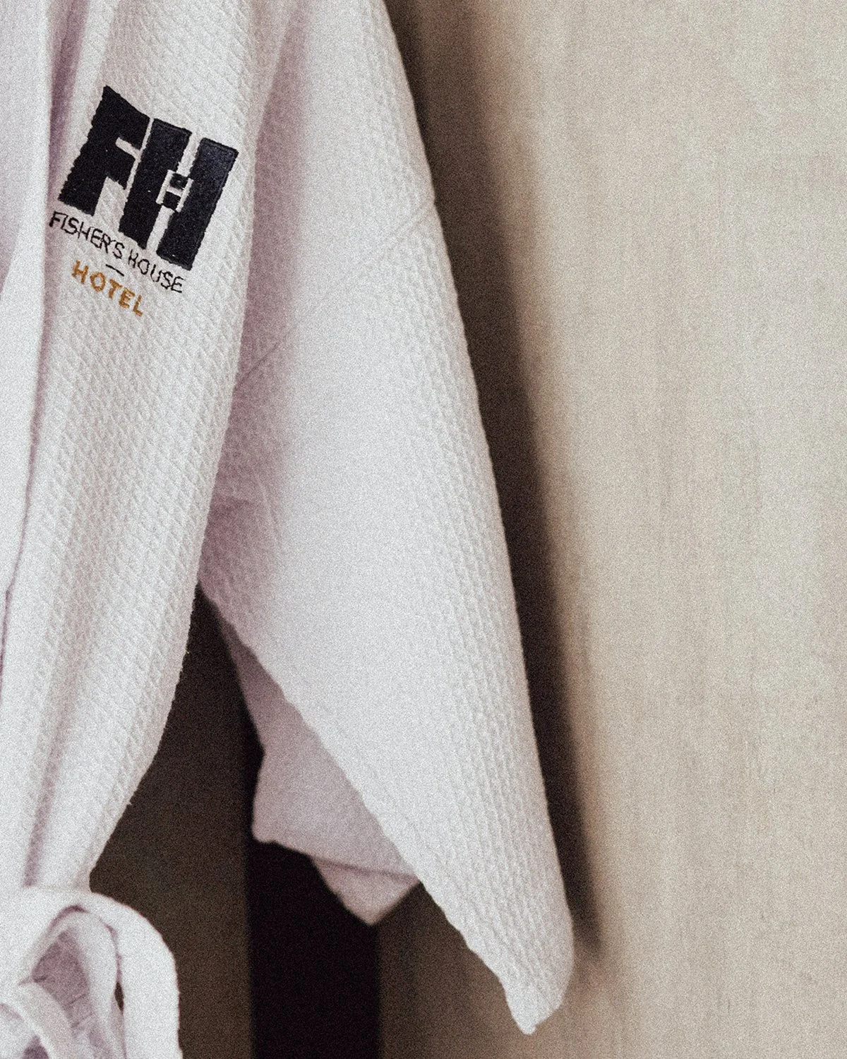 Detalle de una toalla blanca con el logotipo del Fishers House Hotel en negro y naranja.