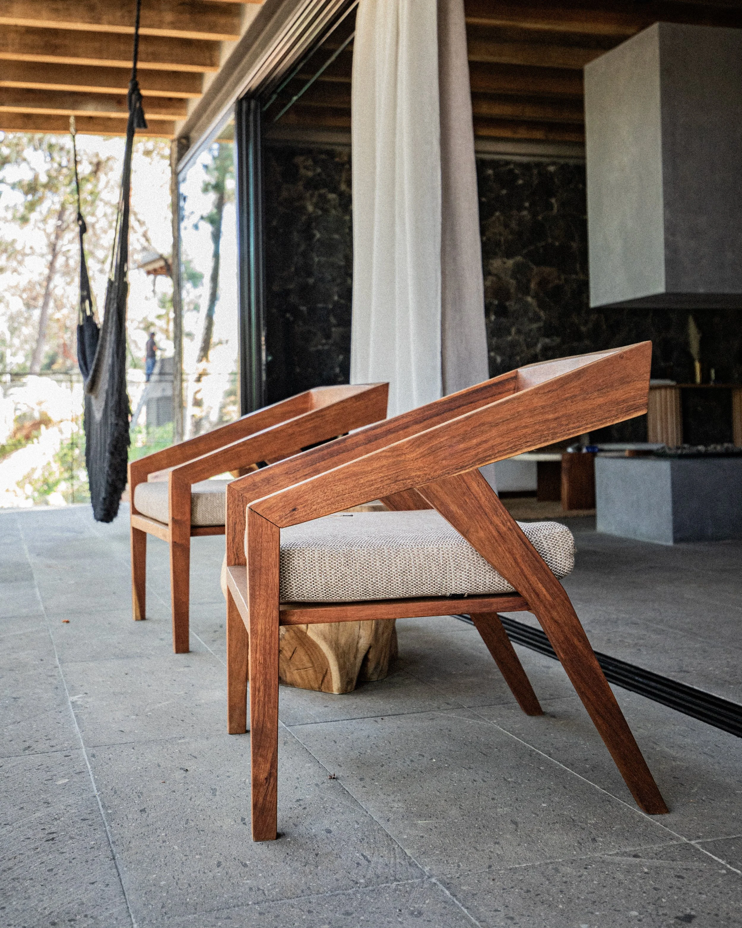 Dos sillas de madera con cojines en una terraza con vista a árboles.