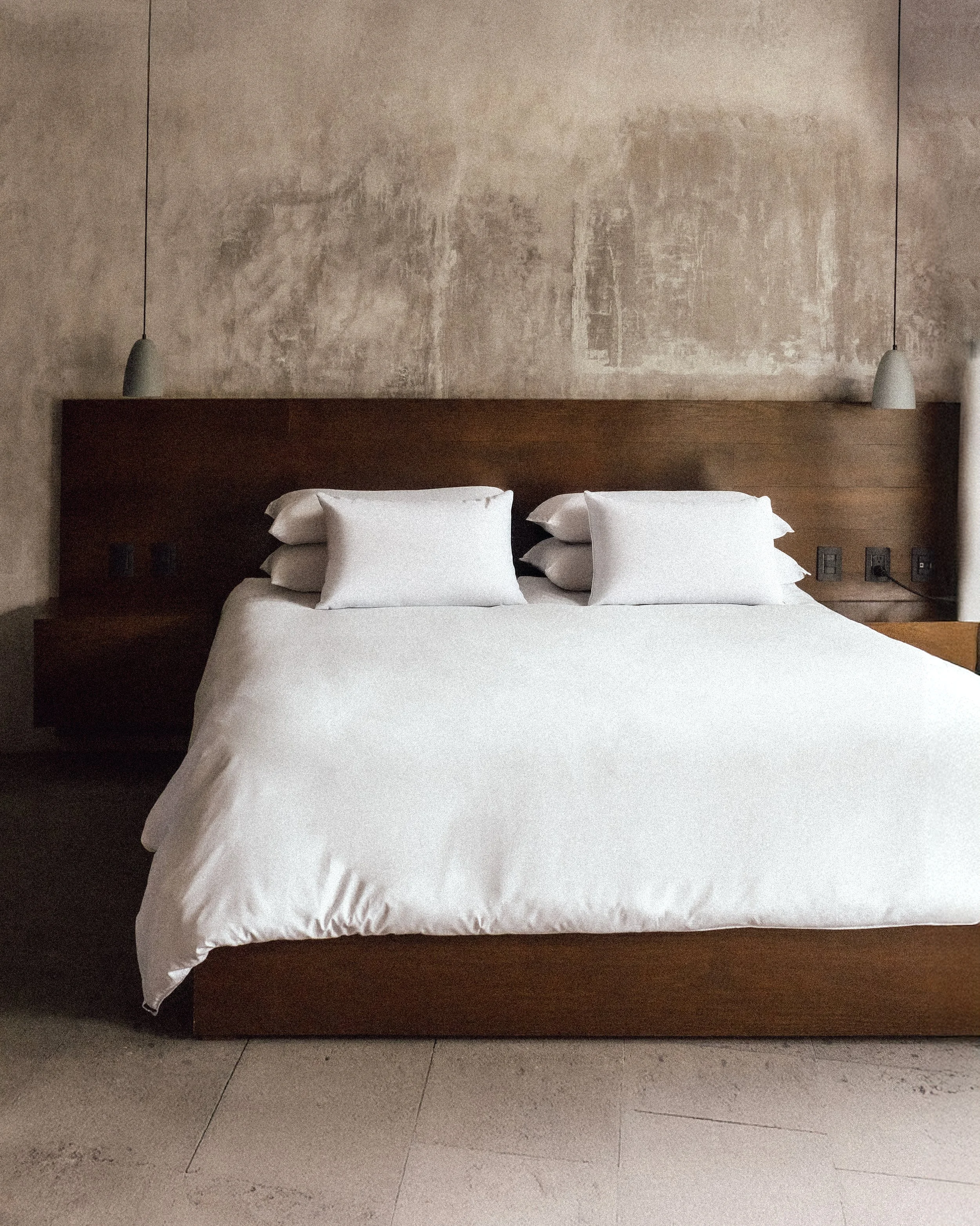 Cama de matrimonio con cabecera de madera y cuatro almohadas blancas, en una habitación moderna.