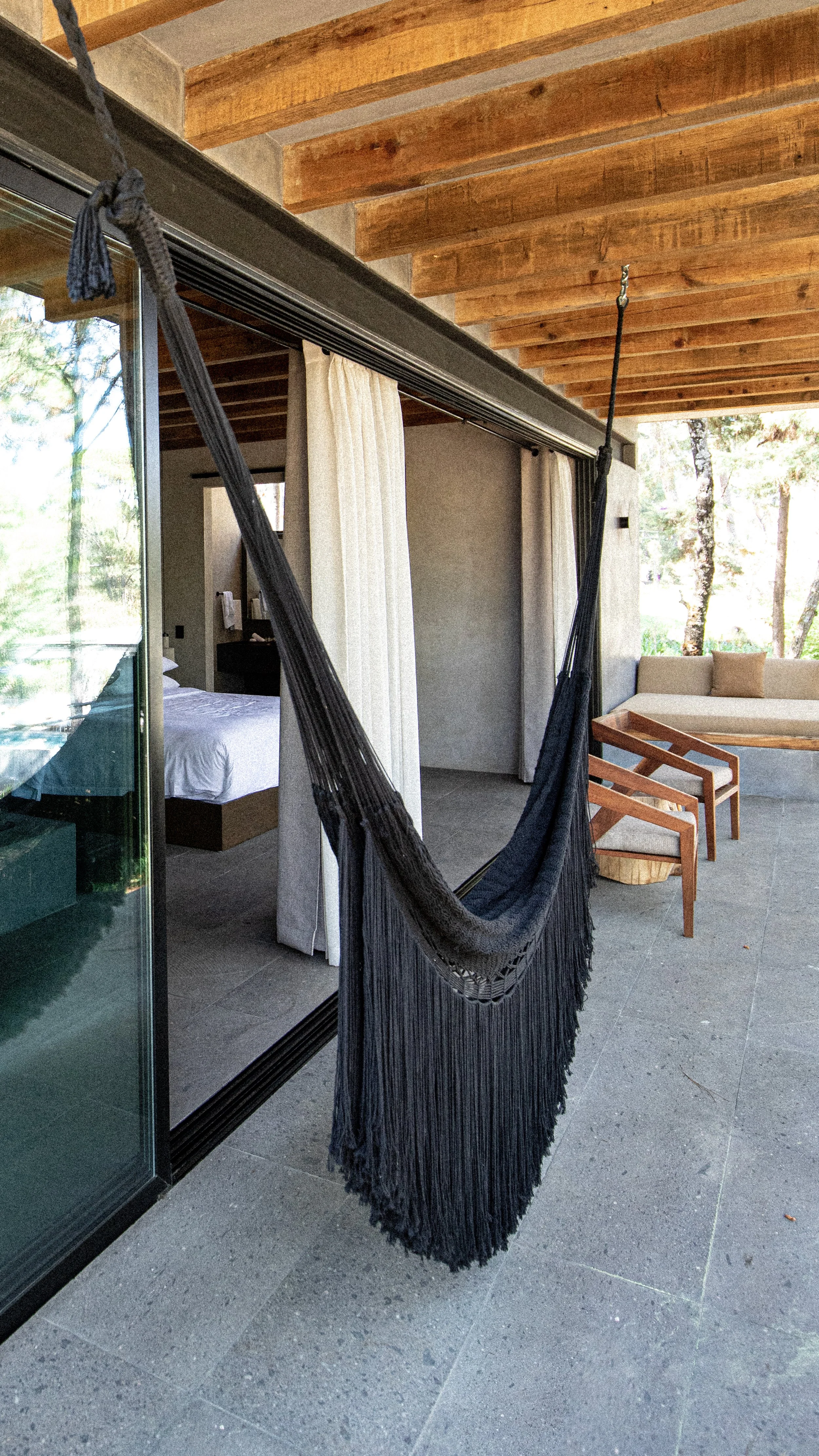 Hamaca negra colgada en un balcón con muebles de madera y vista a un bosque con árboles