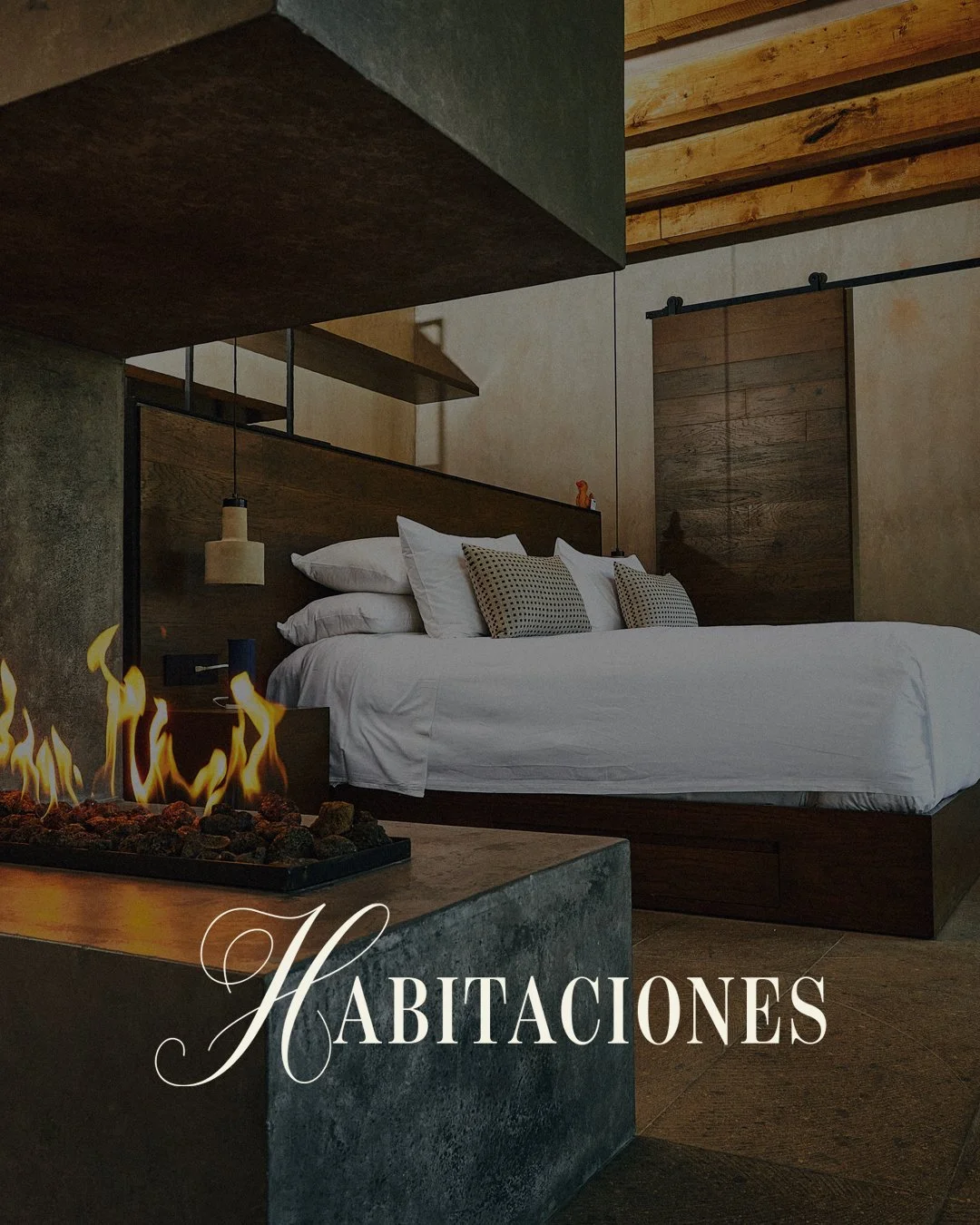 Habitación moderna con cama grande, varios cojines y una chimenea de gas en primer plano.