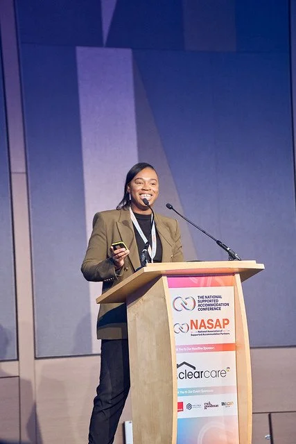 A black woman with a brown blazer speaking on stage.