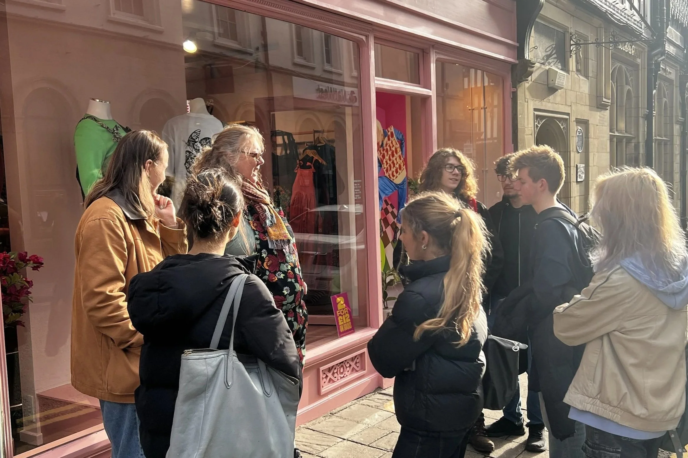 A group of young people standing in front of a pink fashion storefont.