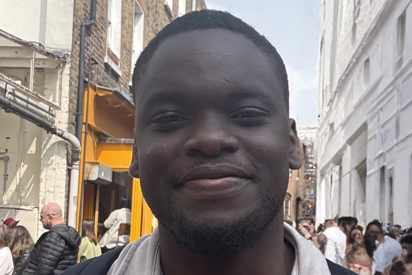 A young black man wearing a grey shirt with backpack.