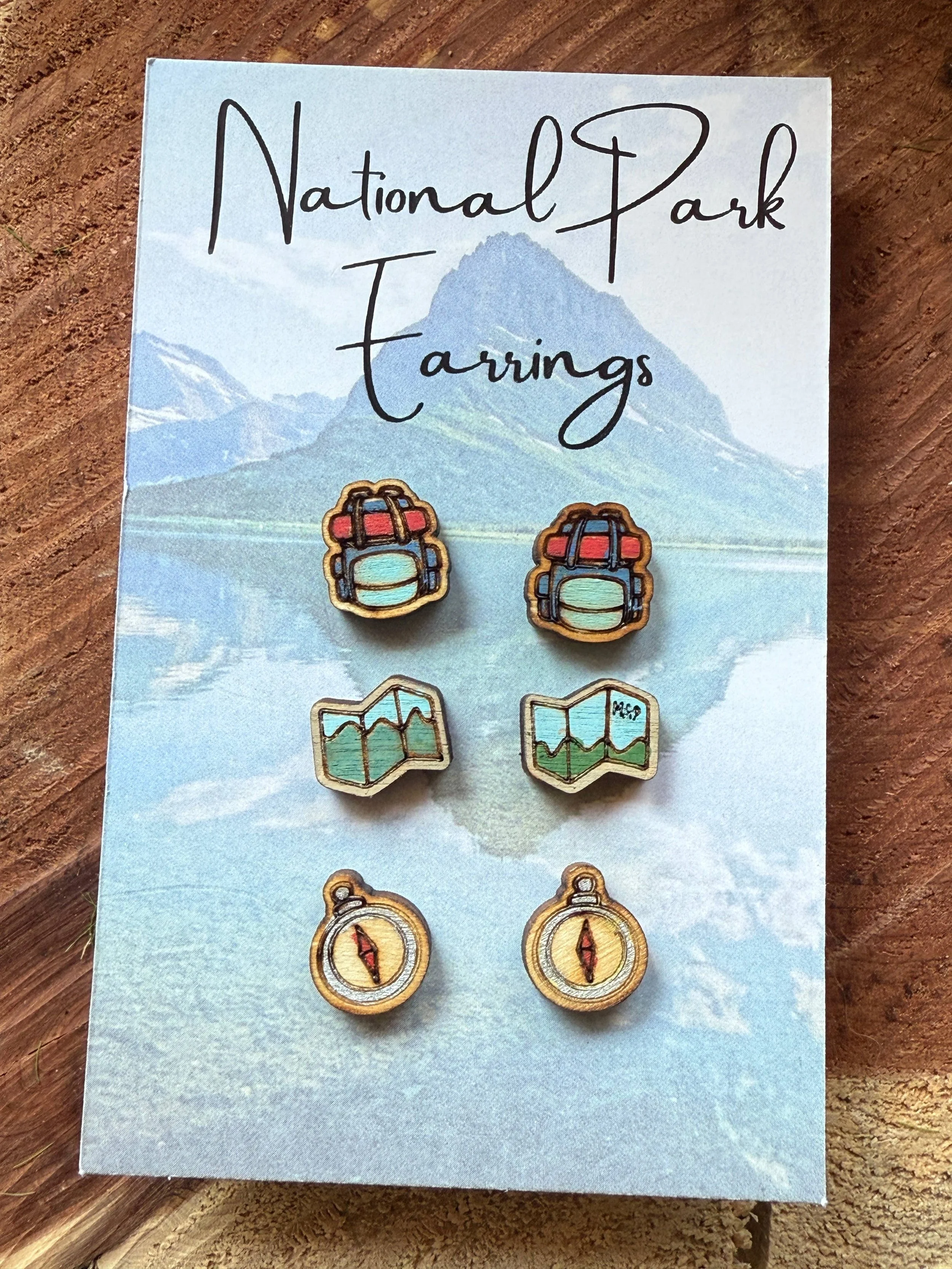 3 pairs of wooden stud earrings. Pair 1 is of a red and blue backpack