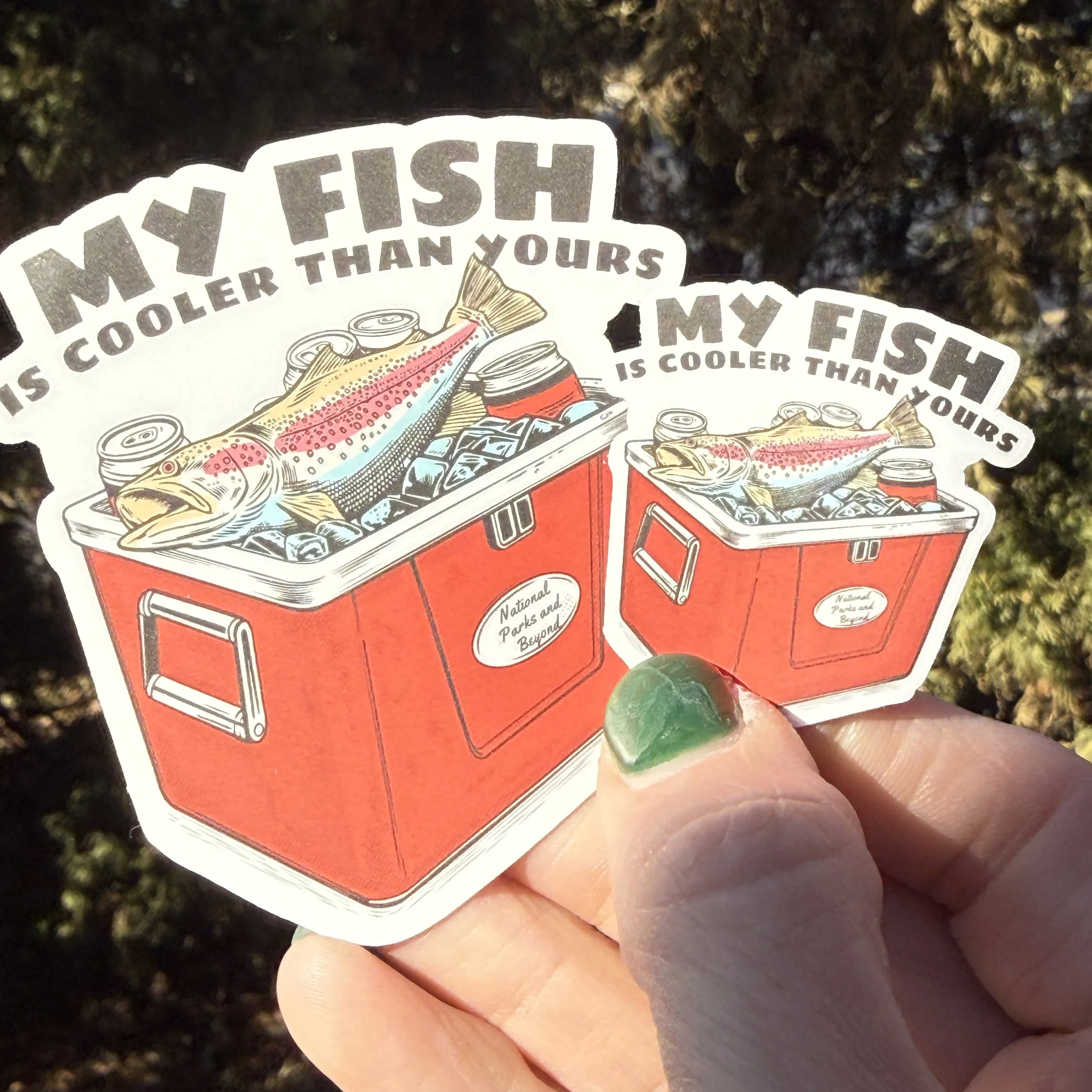 2 inch fishing humor sticker featuring a red hard sided cooler with ice, cans, and a fish on top with the text “My Fish Is Cooler Than Yours”