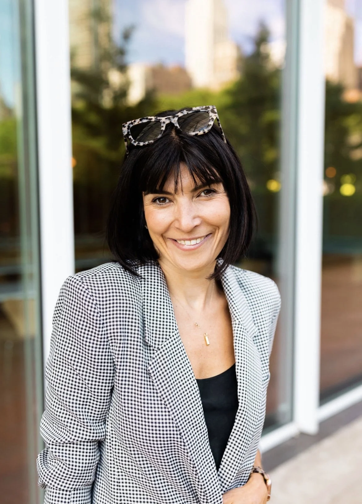 Anna Jones standing in a checked jacket and black tshirt with sunglasses on her head.