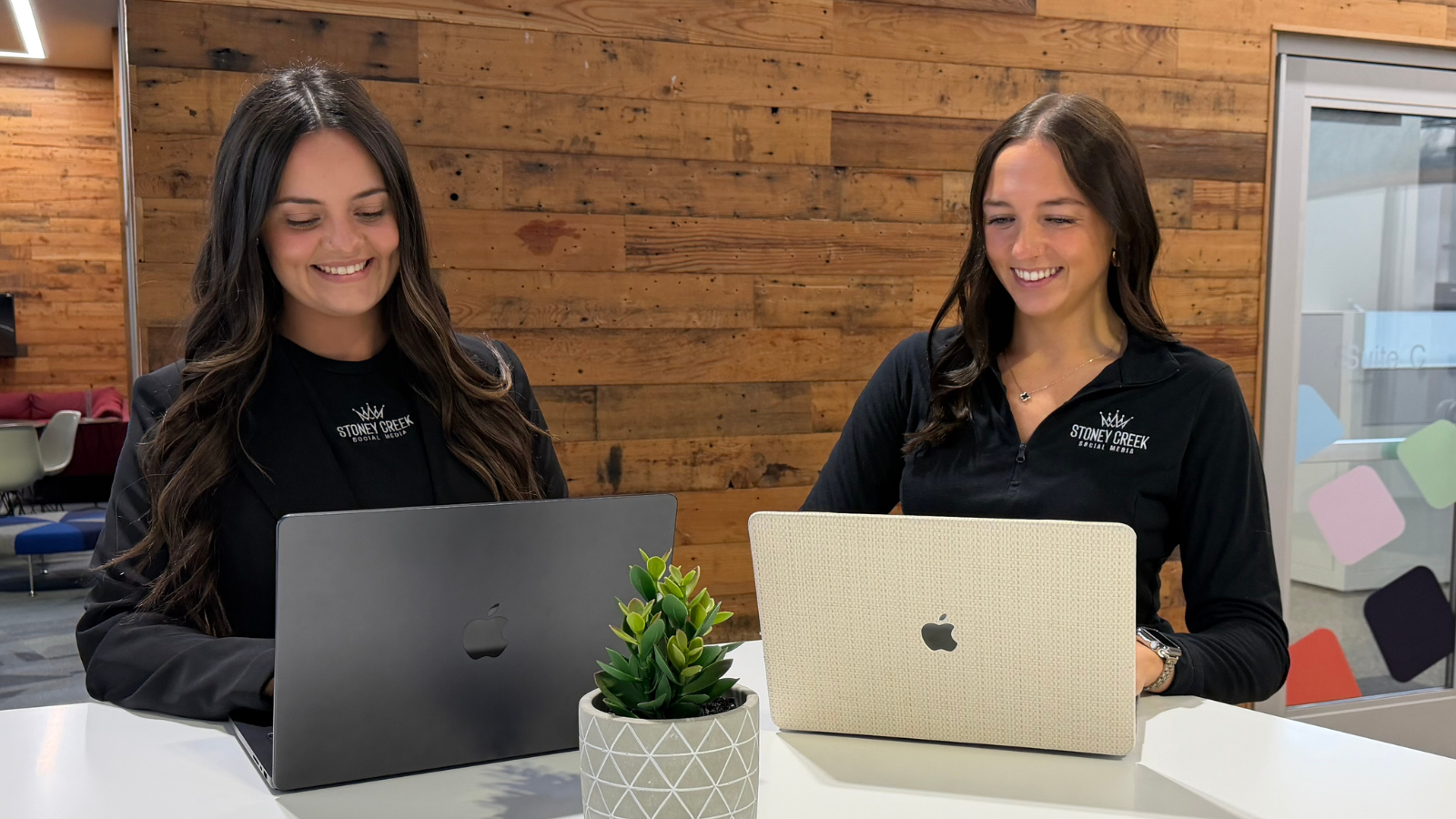 Two Stoney Creek Social Media team members working on laptops in a modern office space, representing paid social media strategy, social media advertising, and digital marketing collaboration.