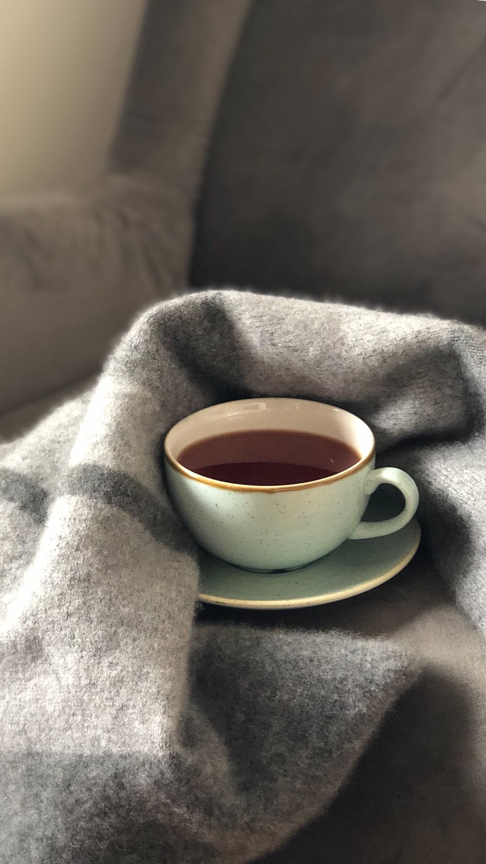 mug of dark liquid against a blanket symbolizing comfort and hygge and my commitment to non-violence in therapy.
