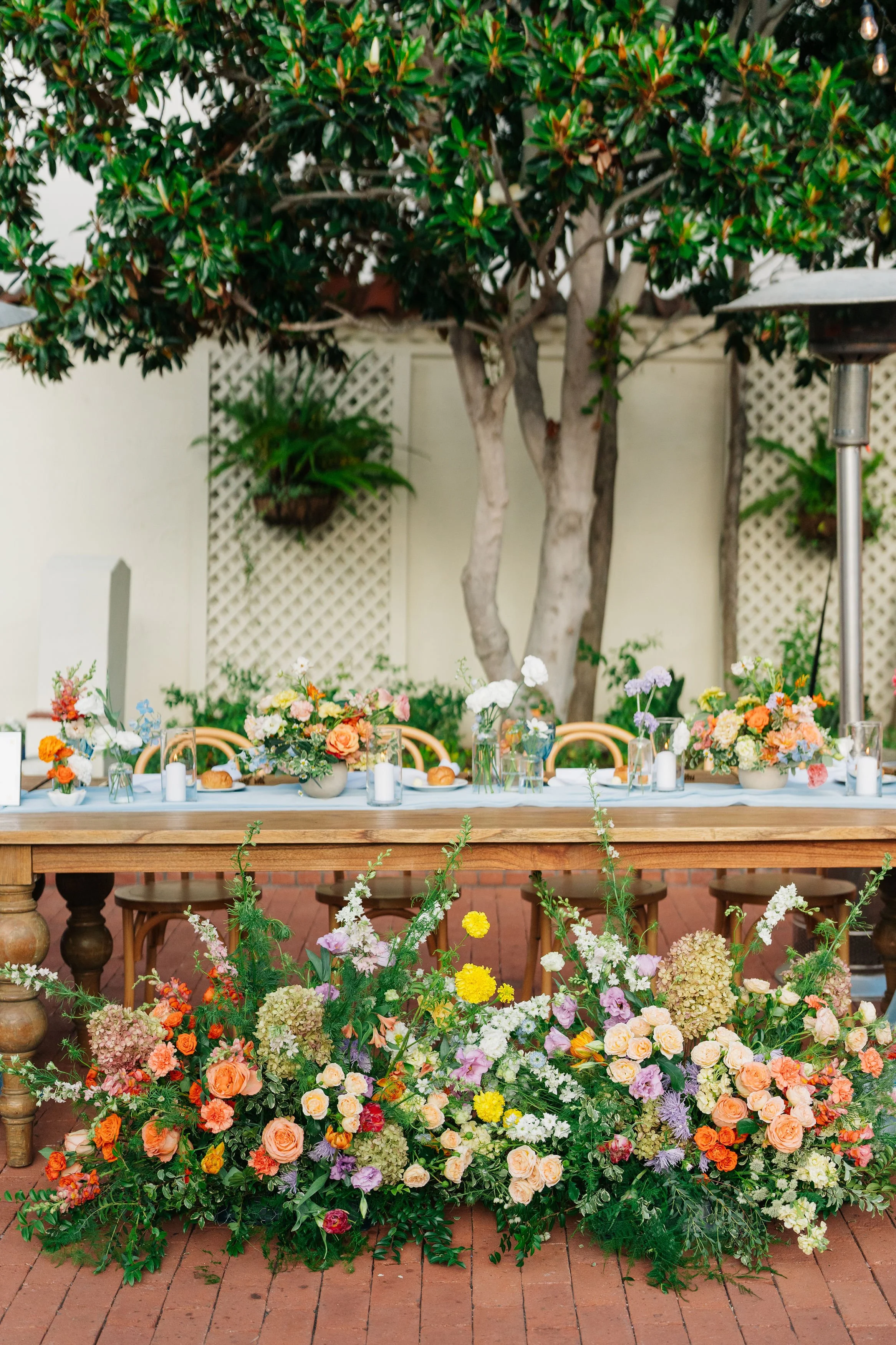 Outdoor floral table arrangement with colorful flowers on a wooden table, surrounded by greenery and trees.