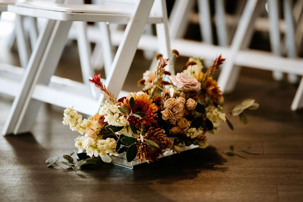 A floral arrangement on the floor near white chairs in a setting likely for a wedding or event.
