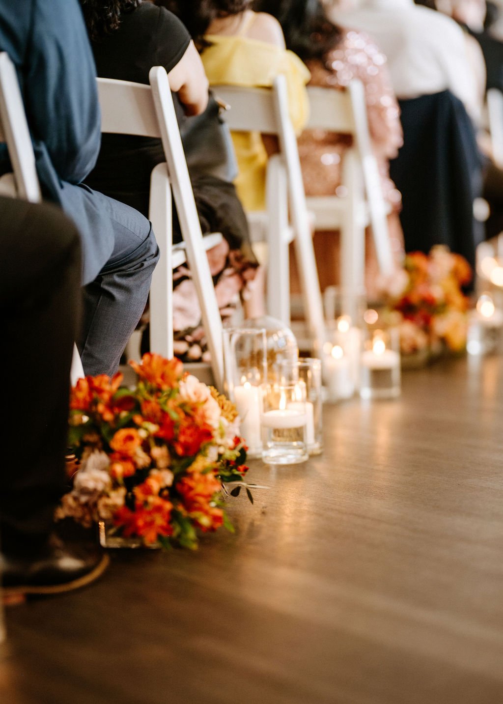 People seated in a row at a wedding ceremony with whimsical aisle floral arrangements and candles on the floor.