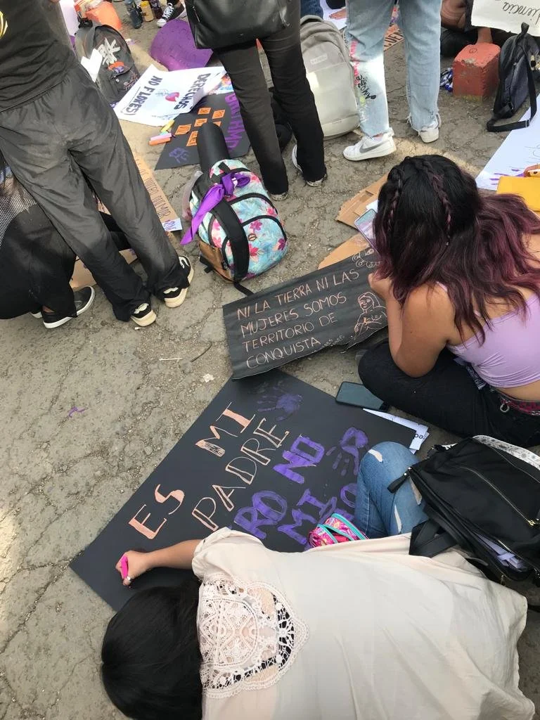 Mujeres jóvenes sentadas en la calle en Cochabamba preparan carteles feministas: "Ni la tierra ni las mujeres somos territorio de conquista"
