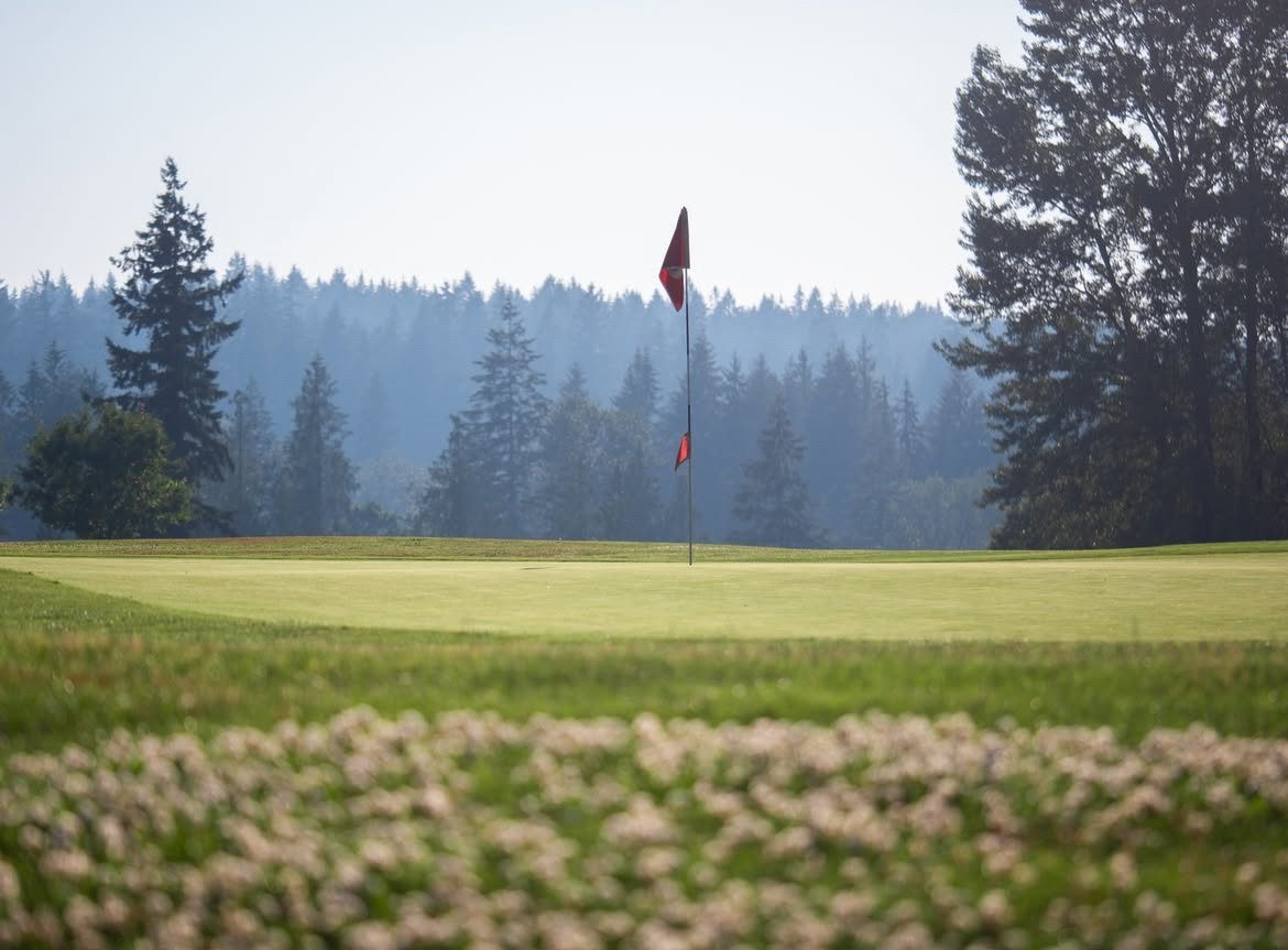Echo Falls Golf Club putting green with red flag pin, surrounded by towering Douglas fir trees in misty Pacific Northwest morning light — Snoqualmie, WA