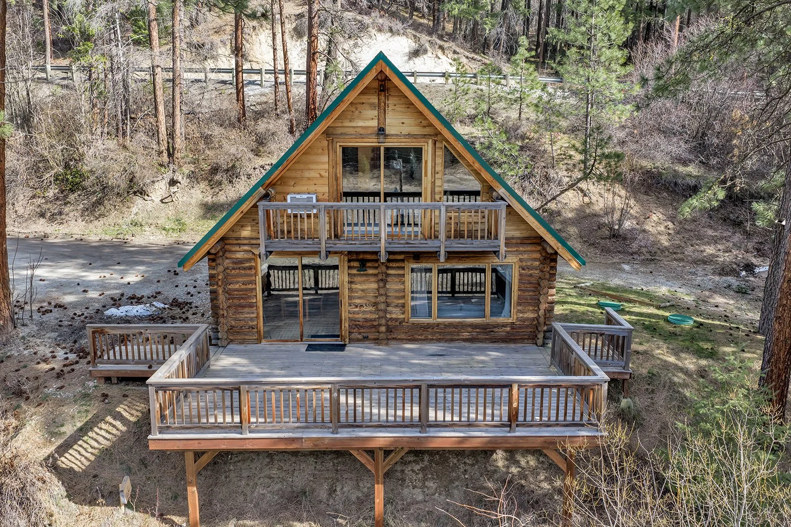 Exterior A-frame log cabin at Pine Vista 17336 Chumstick Hwy Leavenworth WA with large deck creek views and metal roof on 8 private acres near Leavenworth