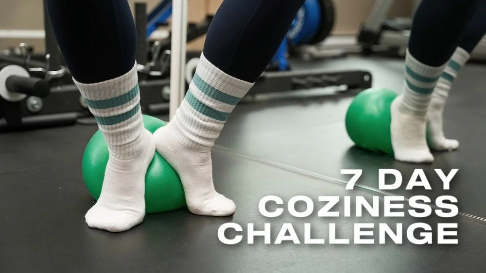 Title card for the 7 Day Coziness Challenge. White text "7 Day Coziness Challenge " on a background of a feet in white tube socks on a pilates ball.