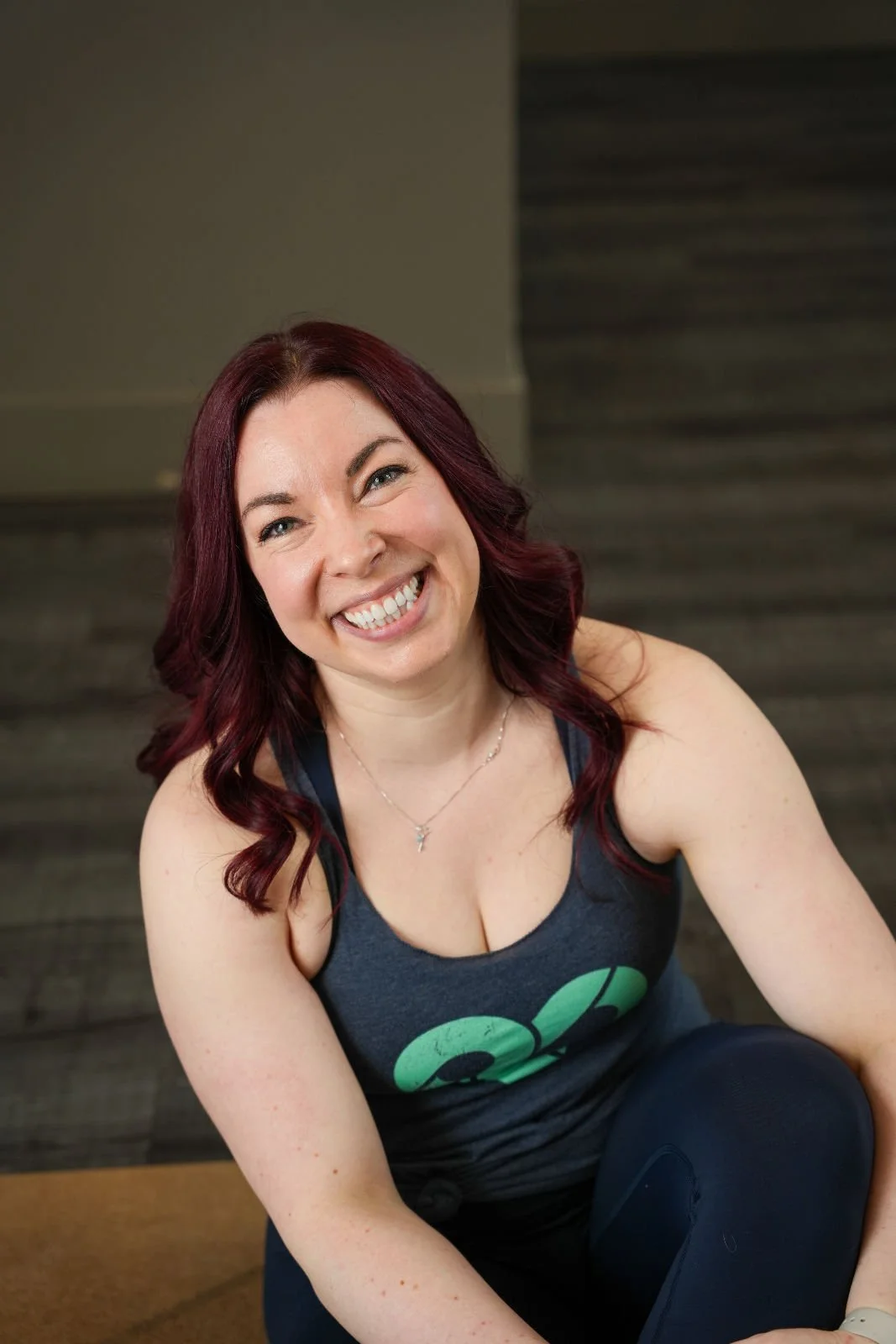 A woman sitting on the ground, with long red hair, and a big, warm smile.