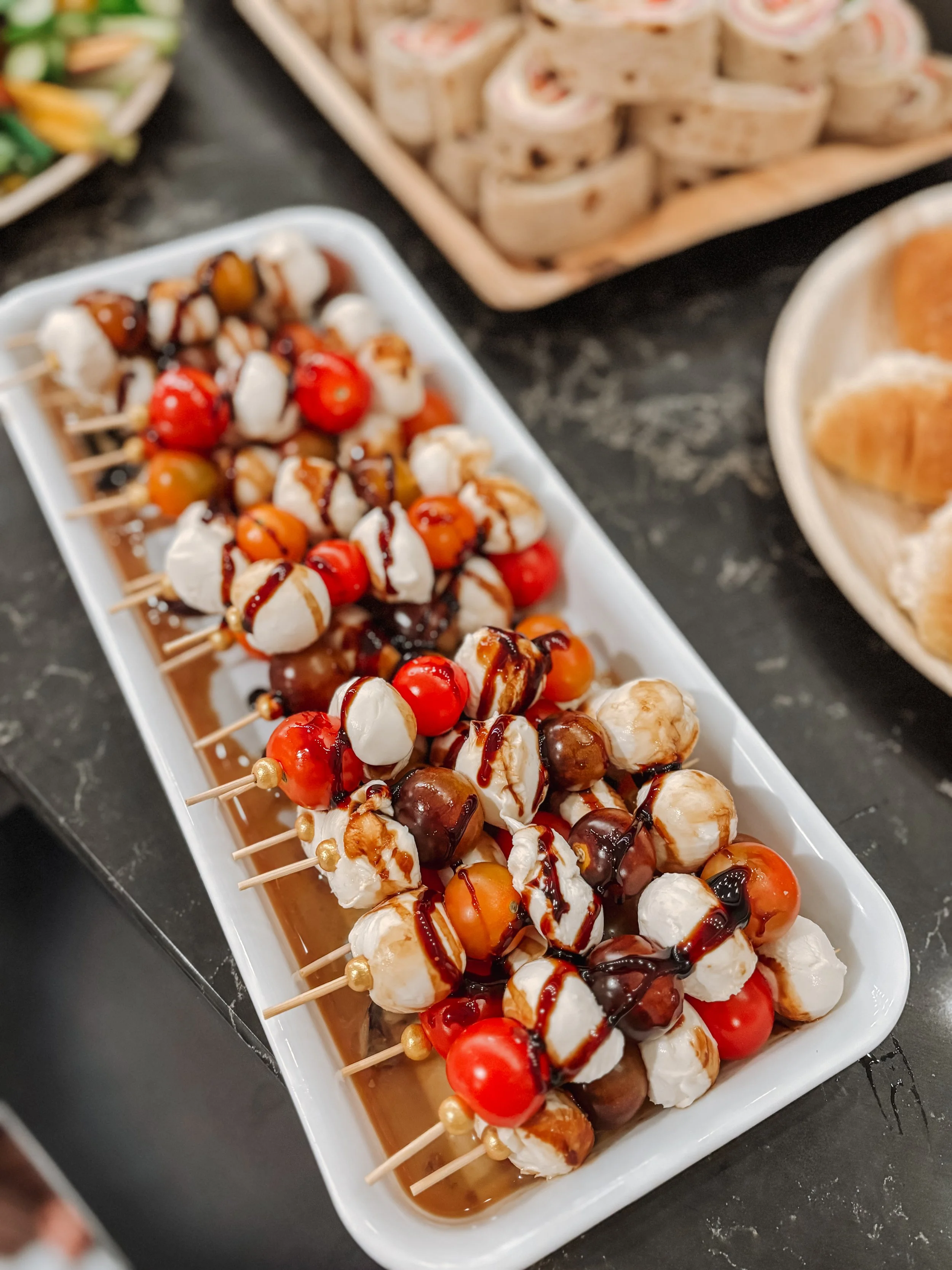 Skewers with mozzarella, cherry tomatoes, and drizzled balsamic glaze on a white platter.
