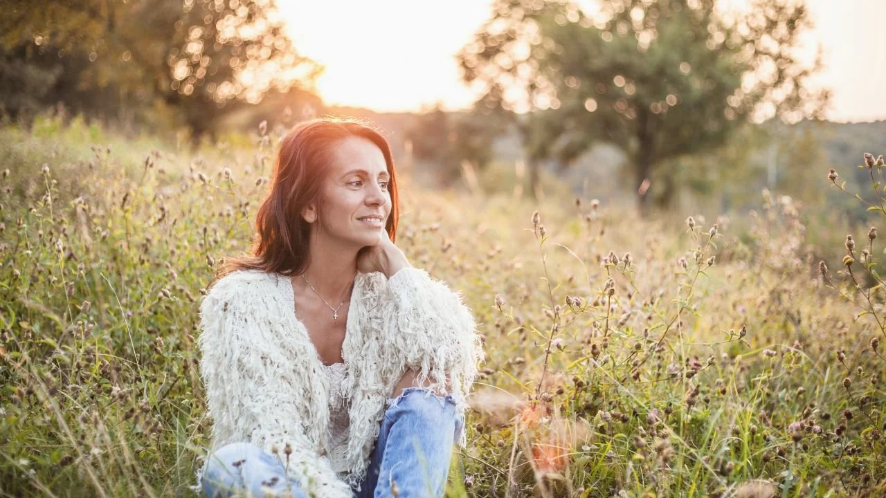 Woman in mid-life sitting in a field looking contemplative