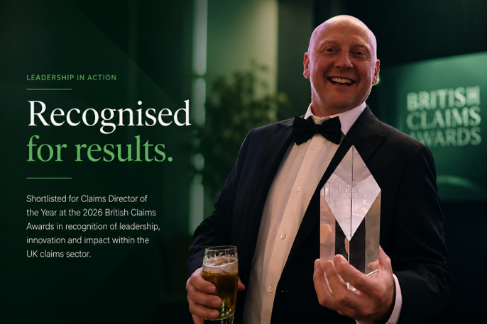 Man in tuxedo holding a glass of beer and a glass award, smiling at an awards ceremony with a dark green backdrop.