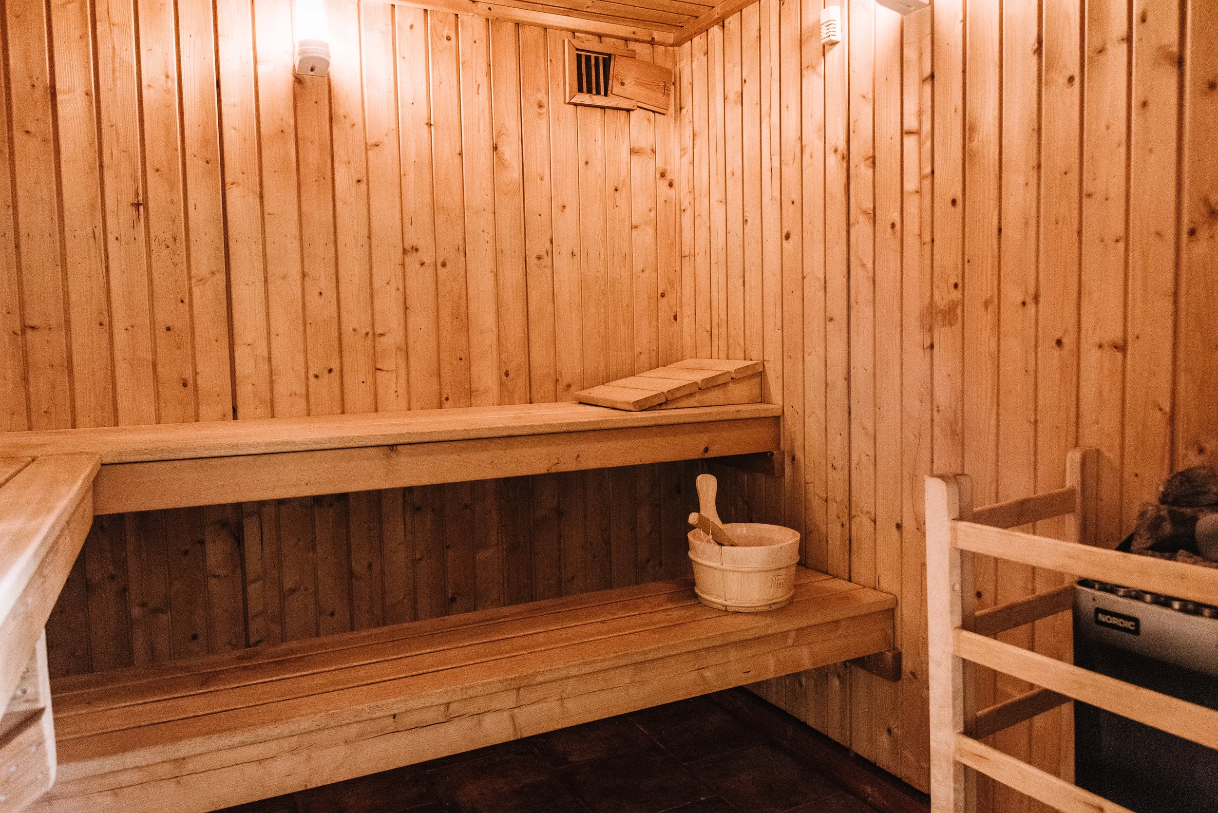 Wood-paneled sauna room with benches, a wooden bucket, and a heater.