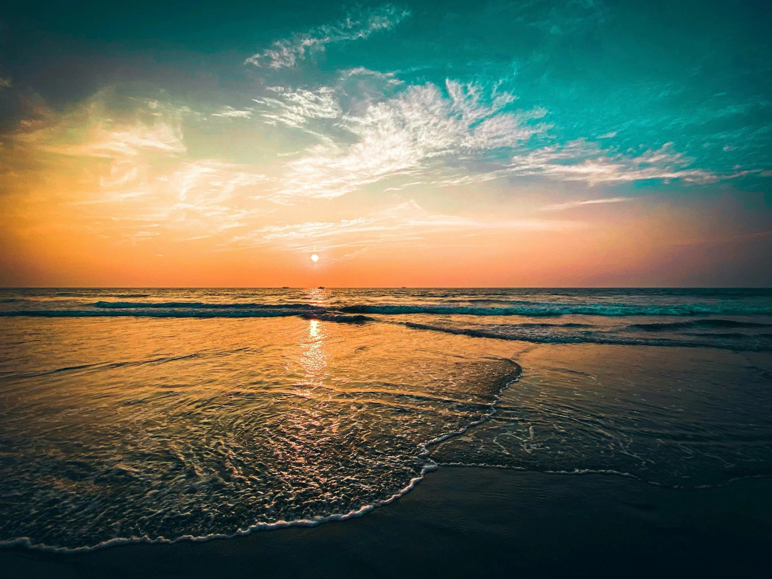 Sun setting over the ocean with colorful sky and waves in the foreground.