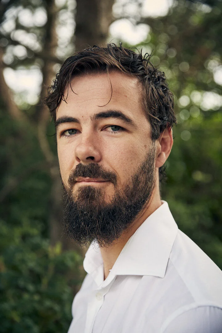 Man with a beard and white shirt in a forest setting