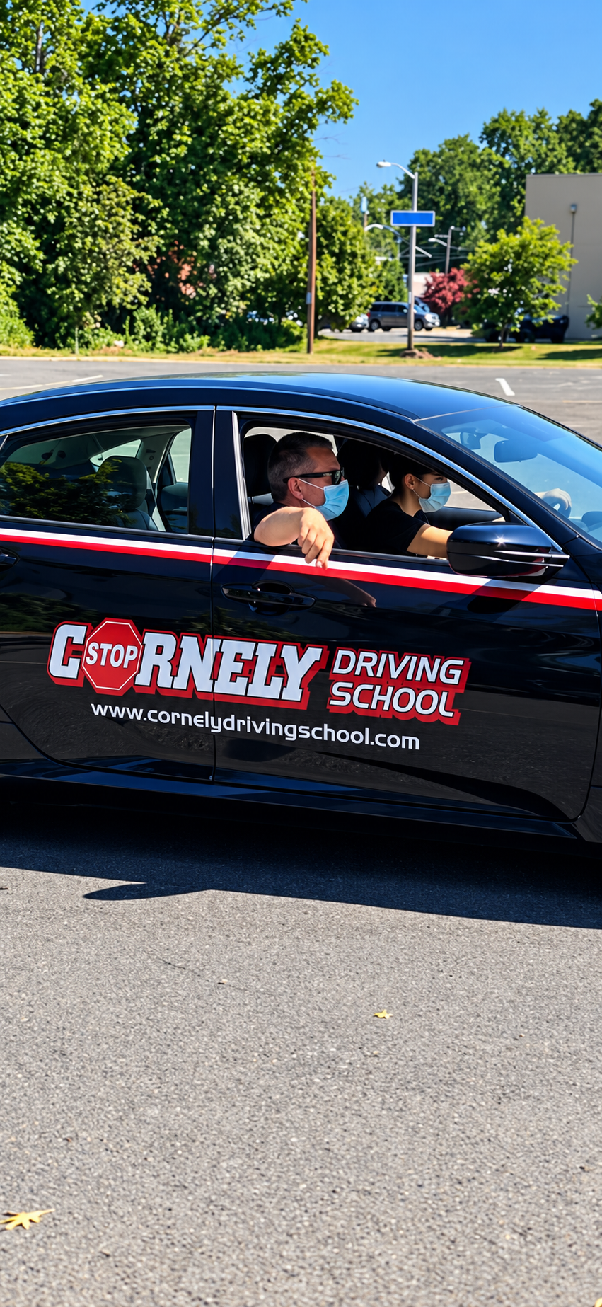 A black car with a 'Cornely Driving School' logo and website, with two people inside wearing masks. The driver is a woman, and the passenger is a man with sunglasses and a mask, sitting with his arm on the window. Behind the car, there are trees and a parking lot.