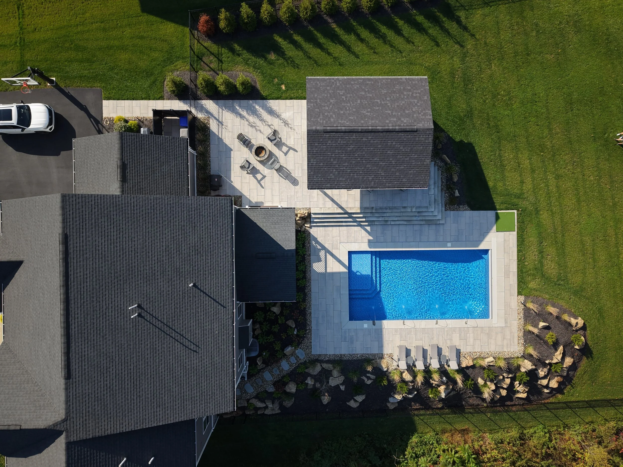 Aerial view of a backyard with a shaded patio area, swimming pool, lawn, and flower garden.