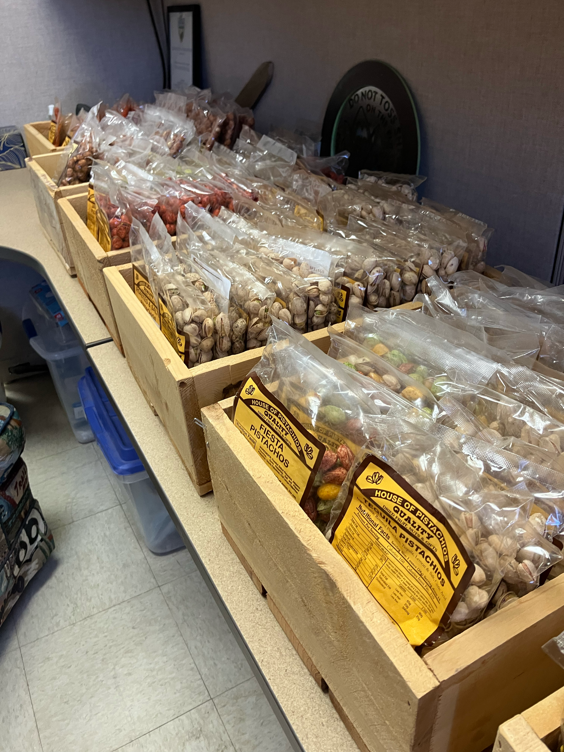 Several bags of pistachios in different varieties and flavors displayed on wooden shelves in a store.