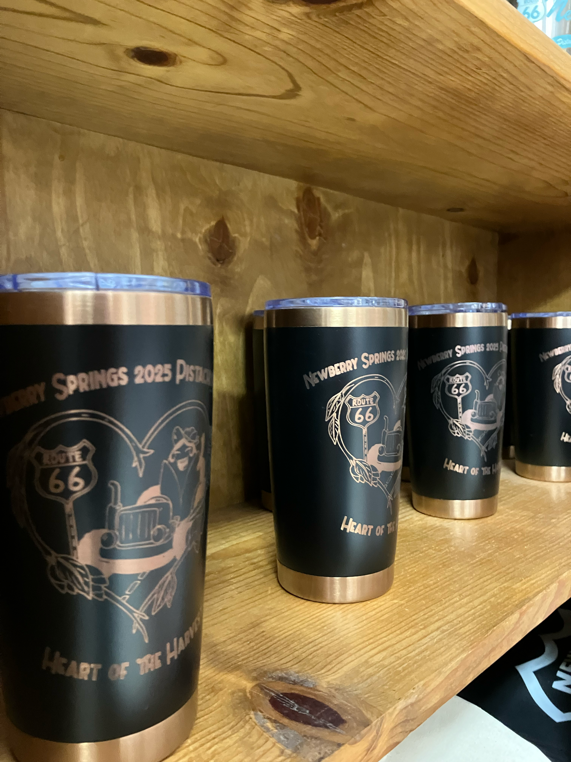 Four black and copper-colored cans with Route 66 and Route 66 Heart of the Heart of the Land printed on them, lined up on a wooden surface.