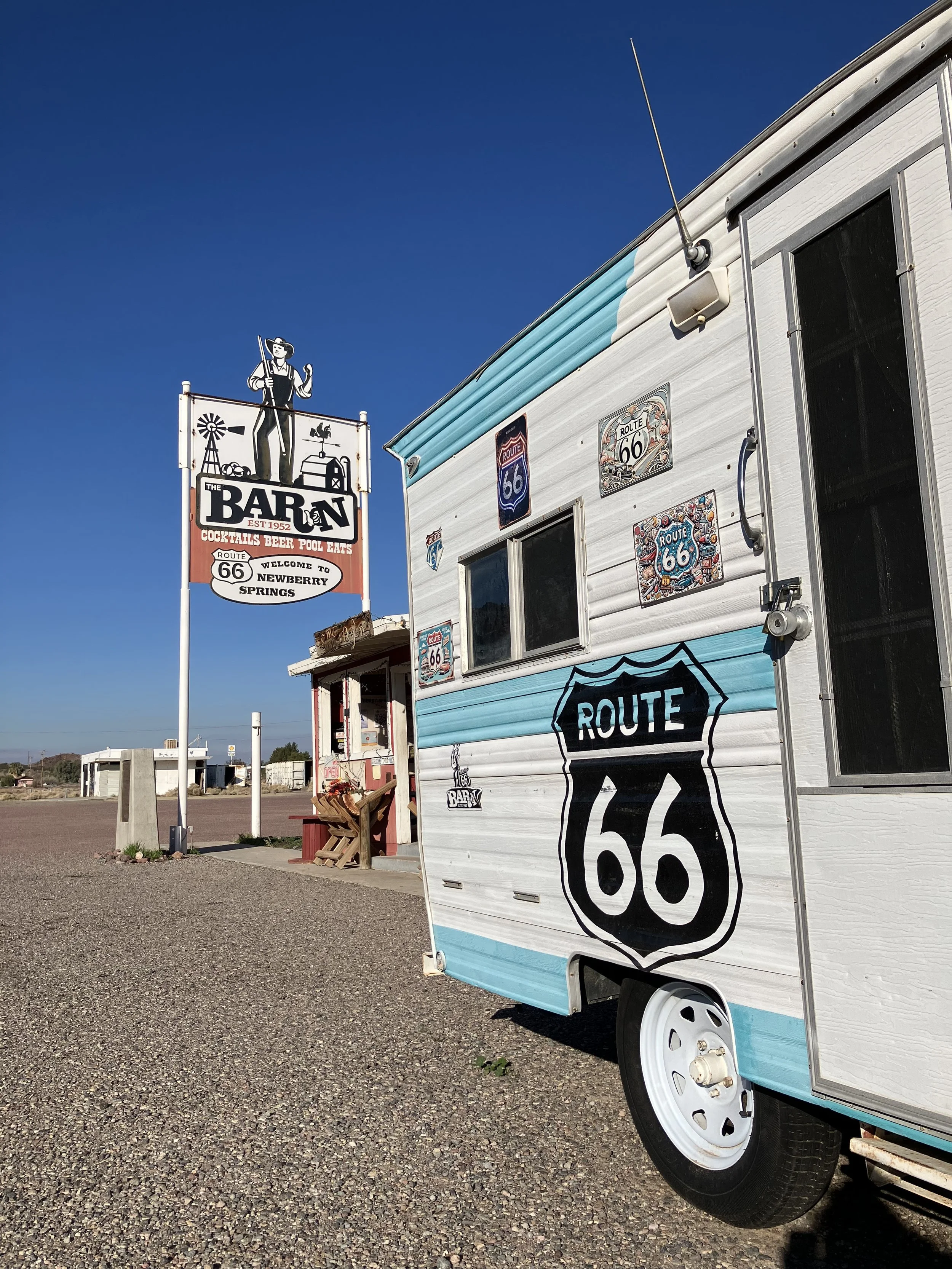 A white and blue trailer with Route 66 signs parked outside a bar on a sunny day, with a clear blue sky.