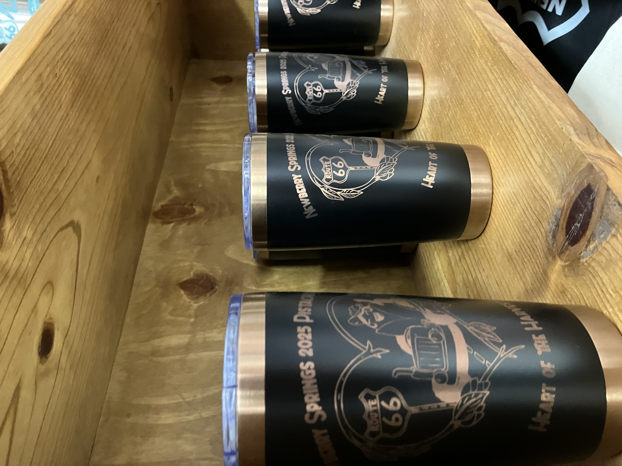 Four black and copper-colored cans with Route 66 and Route 66 Heart of the Heart of the Land printed on them, lined up on a wooden surface.