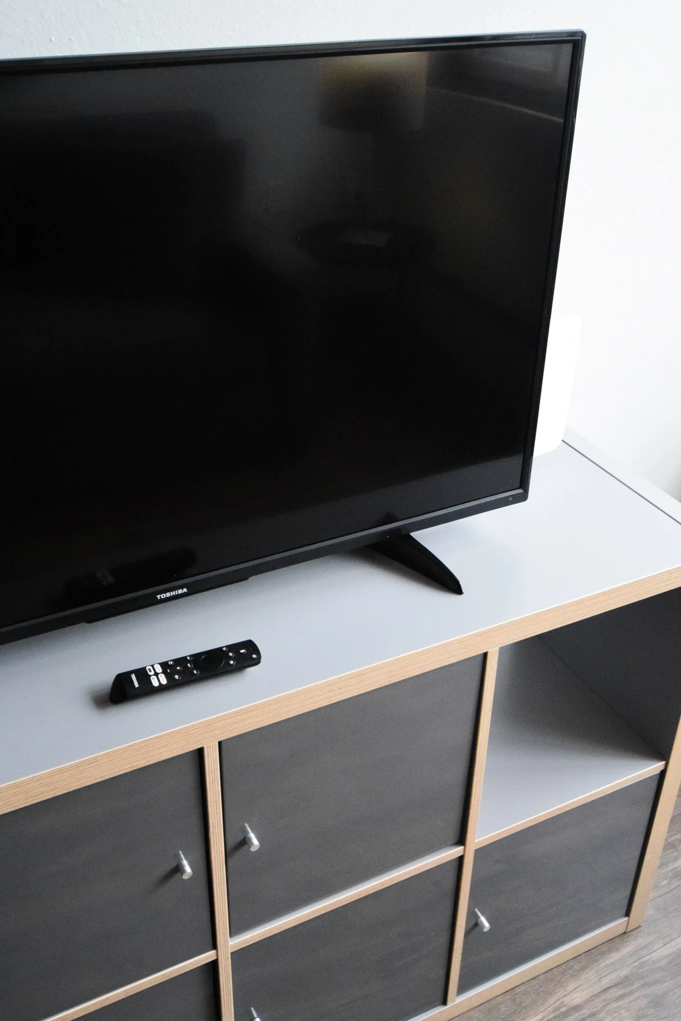 A black television on a white and wood cabinet with a remote control placed on the surface.