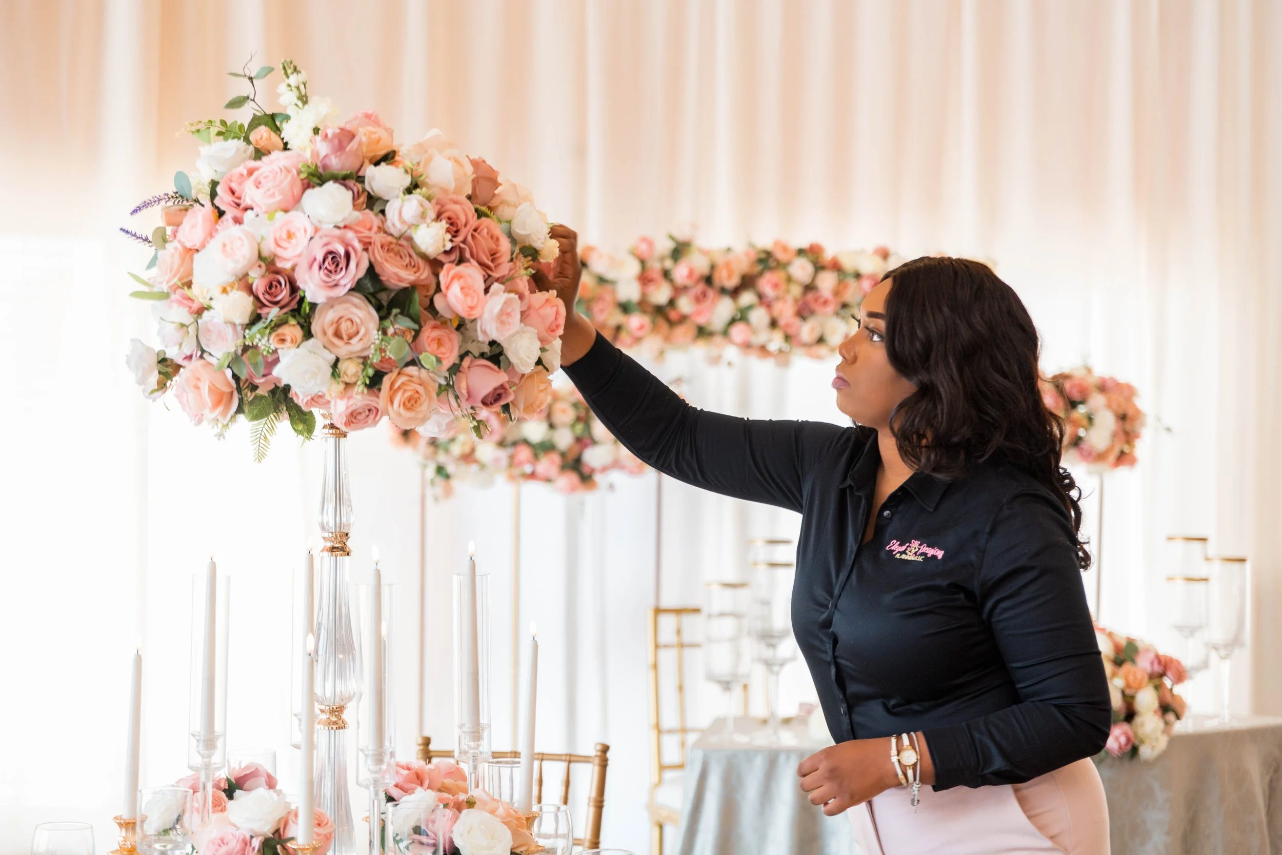 A woman arranging a bouquet of pink and white roses on a wedding or event table