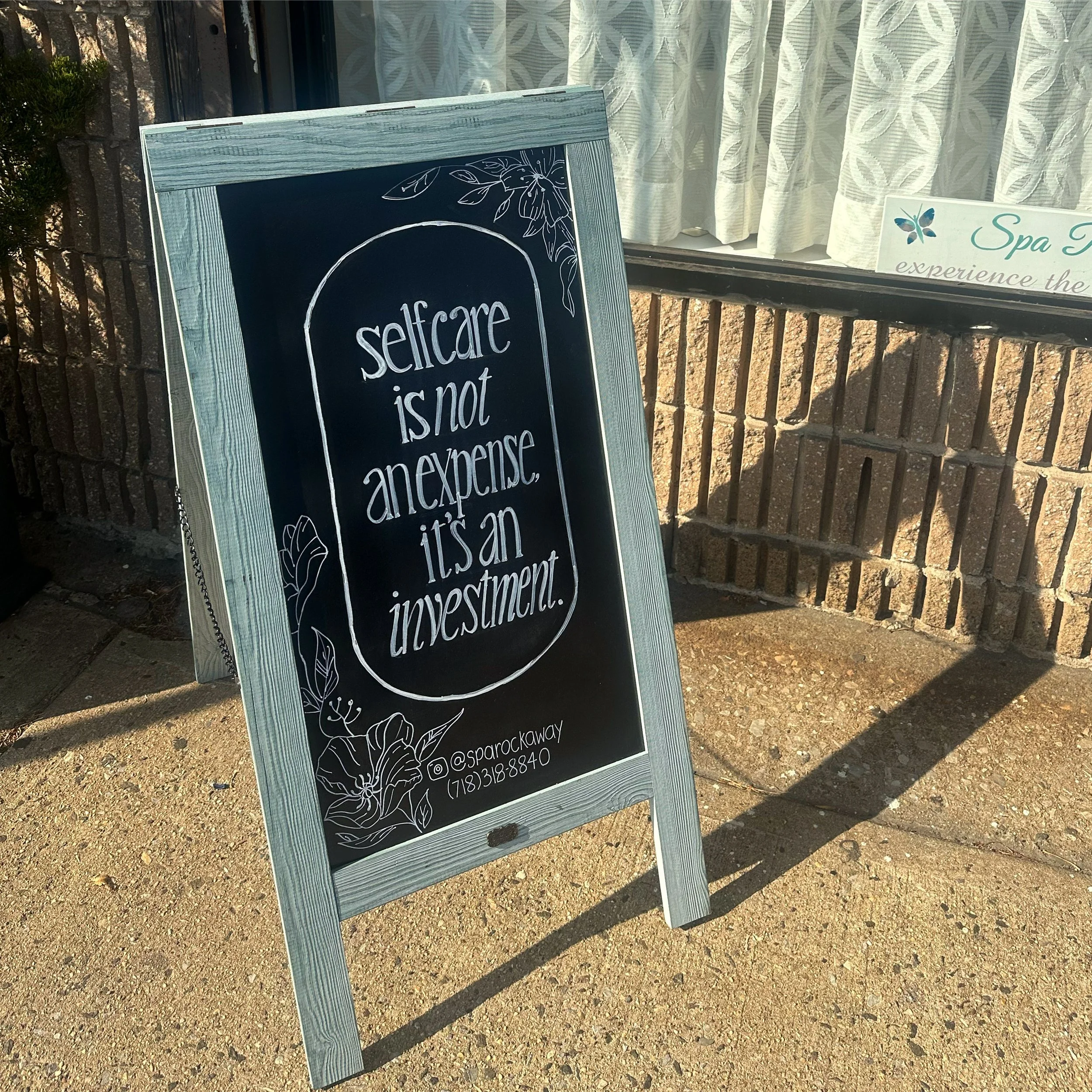Chalkboard sign in front of Spa Rockaway with flowers and "Self care is not an expense, it's an investment."