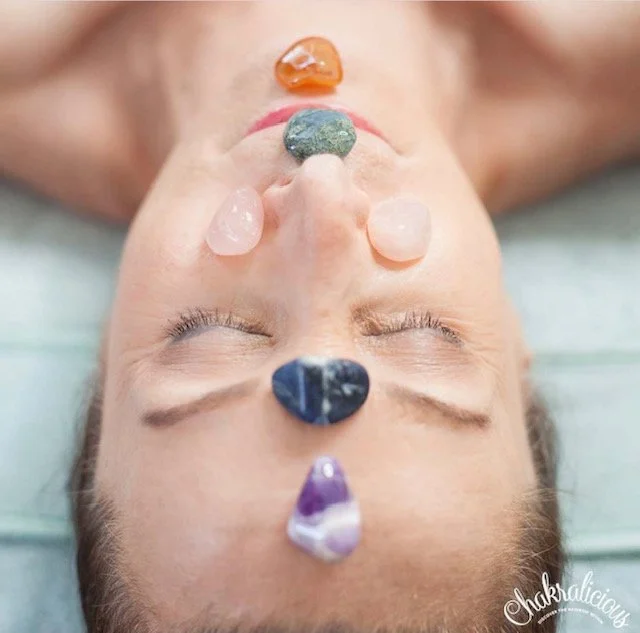 Woman laying with eyes closed with gemstones/polished rocks on her face