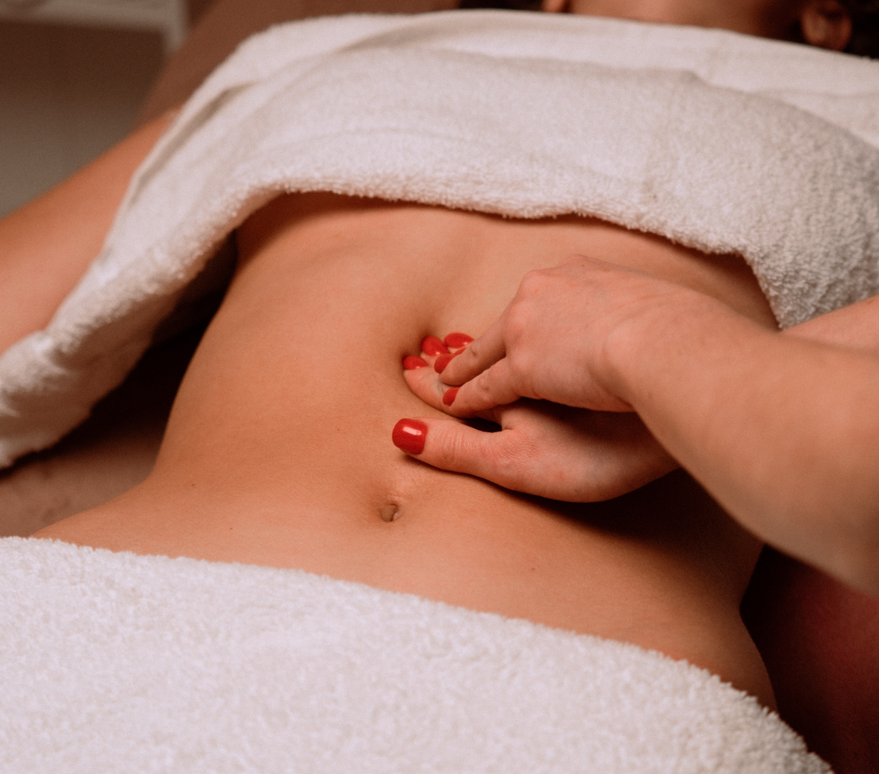 Close-up of a practitioner assessing the abdominal wall by gently pressing near the navel, demonstrating techniques used for core engagement and diastasis recti evaluation in a wellness or Pilates setting.