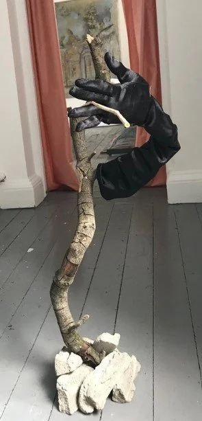 Branched gloved hand rising from the rubble. (broken cement stones, branch, satin glove, bullrush stem) Height 80cm x 30cm (2022)