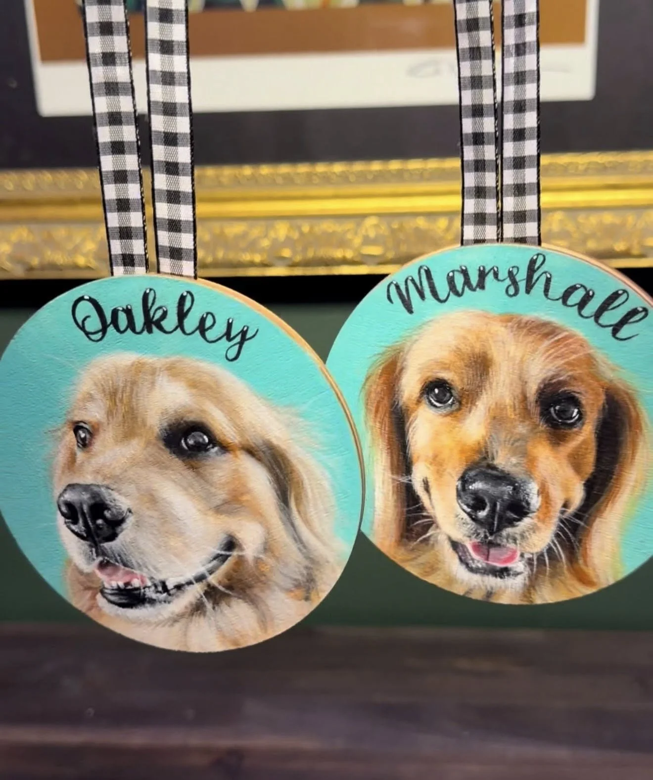 Decorative hanging ornaments featuring realistic painted portraits of two dogs, labeled 'Oakley' and 'Marshall', with gingham ribbon holders.