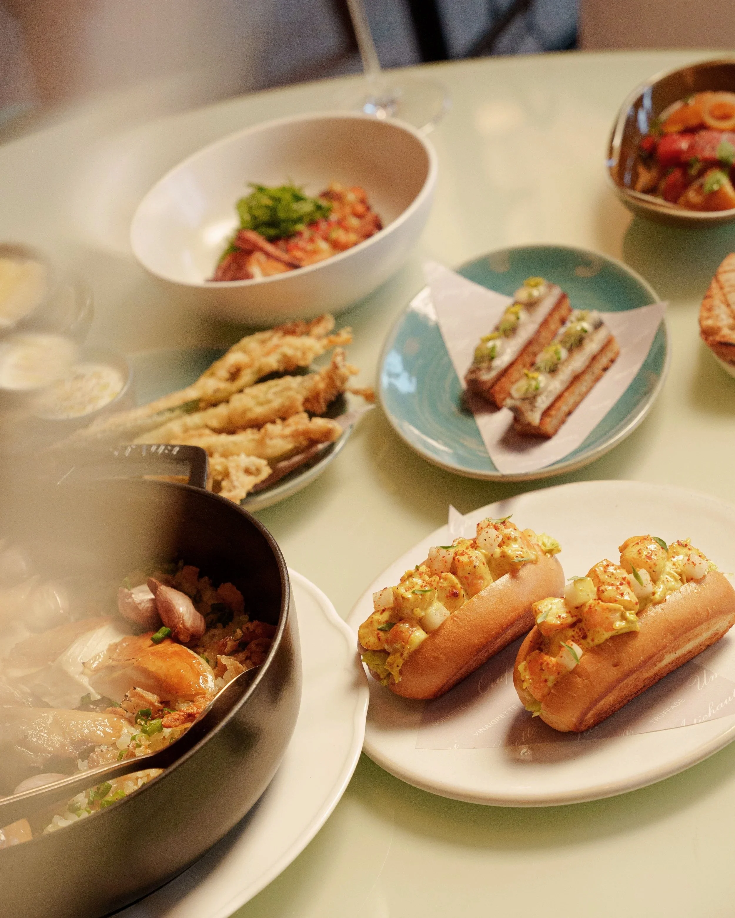 Assorted dishes including hot dogs with chopped onions and relish, fried food, salad, and other small plates on a dining table.
