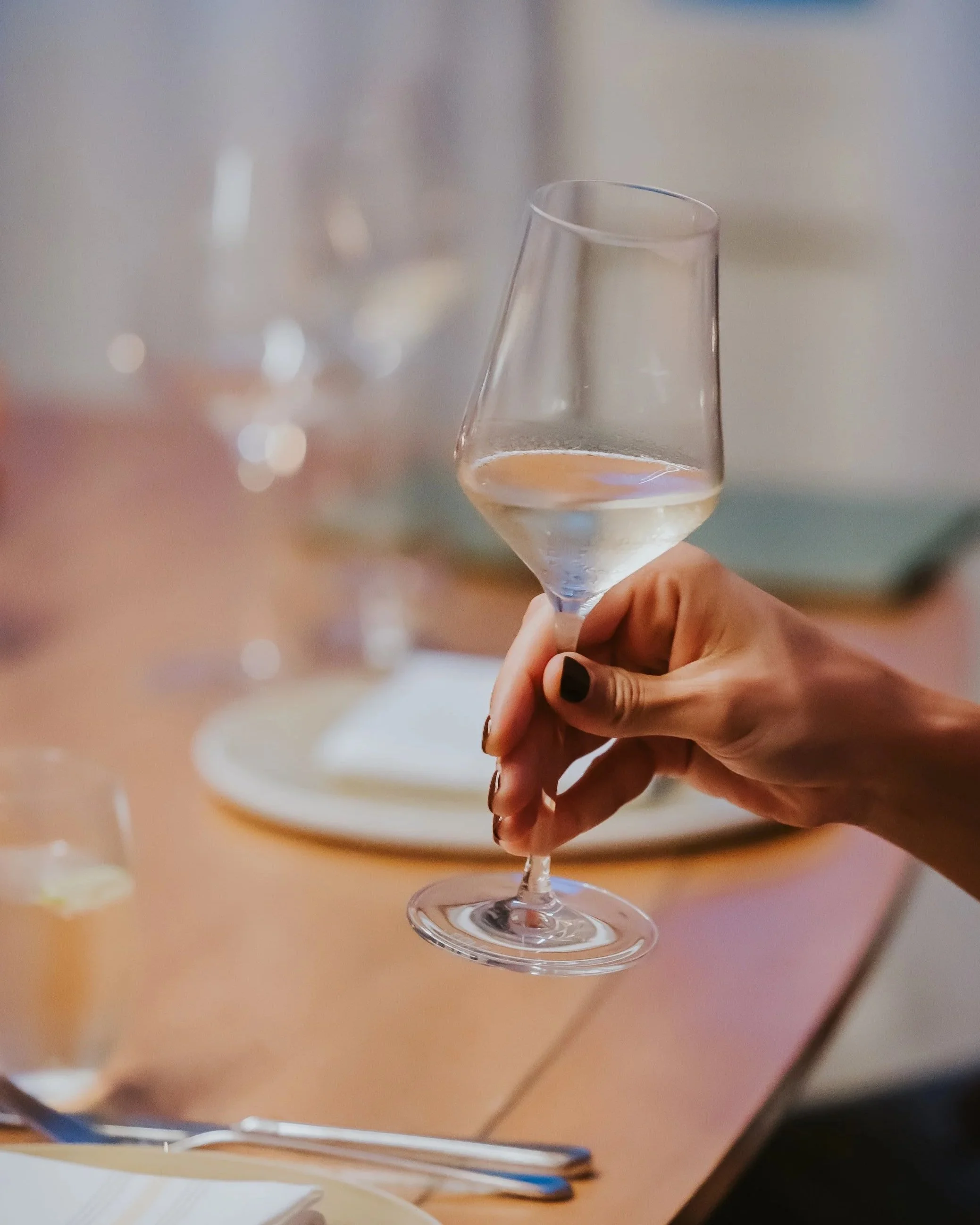 A person holding a glass of white wine in a restaurant setting.