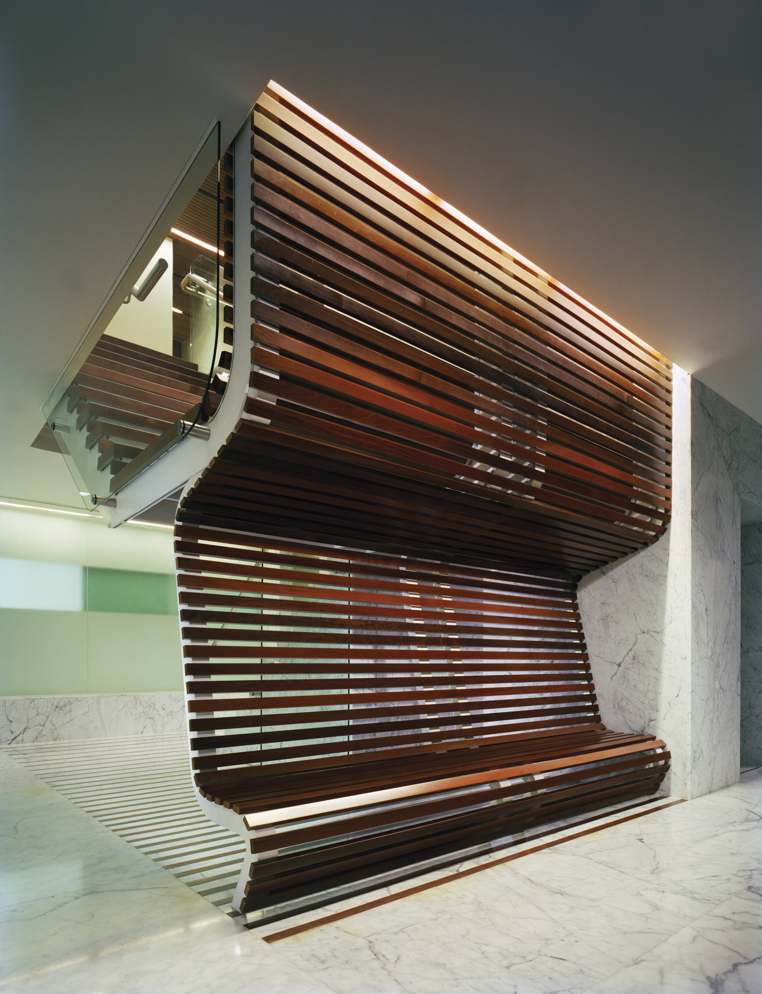 JGNA spa with a sculptural curved wood-slat bench set against white marble walls